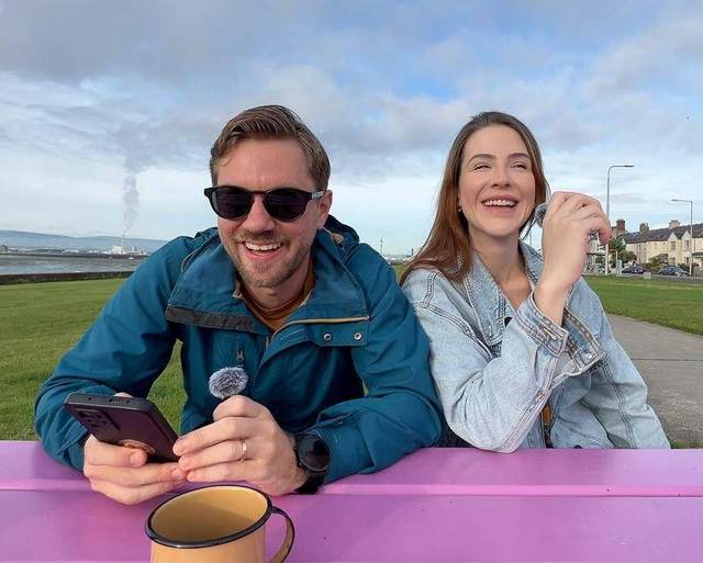 Renato e Luiza sorrindo numa mesa de piquenique à beira-mar em Dublin